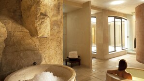Un espace de bien-être doté d’un mur en pierre, d’un grand récipient rempli de glace, d’une baignoire en bois et d’une cabine de douche en verre.