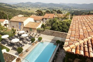 A pool area with lounge chairs and umbrellas, surrounded by terracotta-roofed buildings and lush greenery. - Maison Bérard – hôtel restaurant spa (La Cadiere-d'Azur)