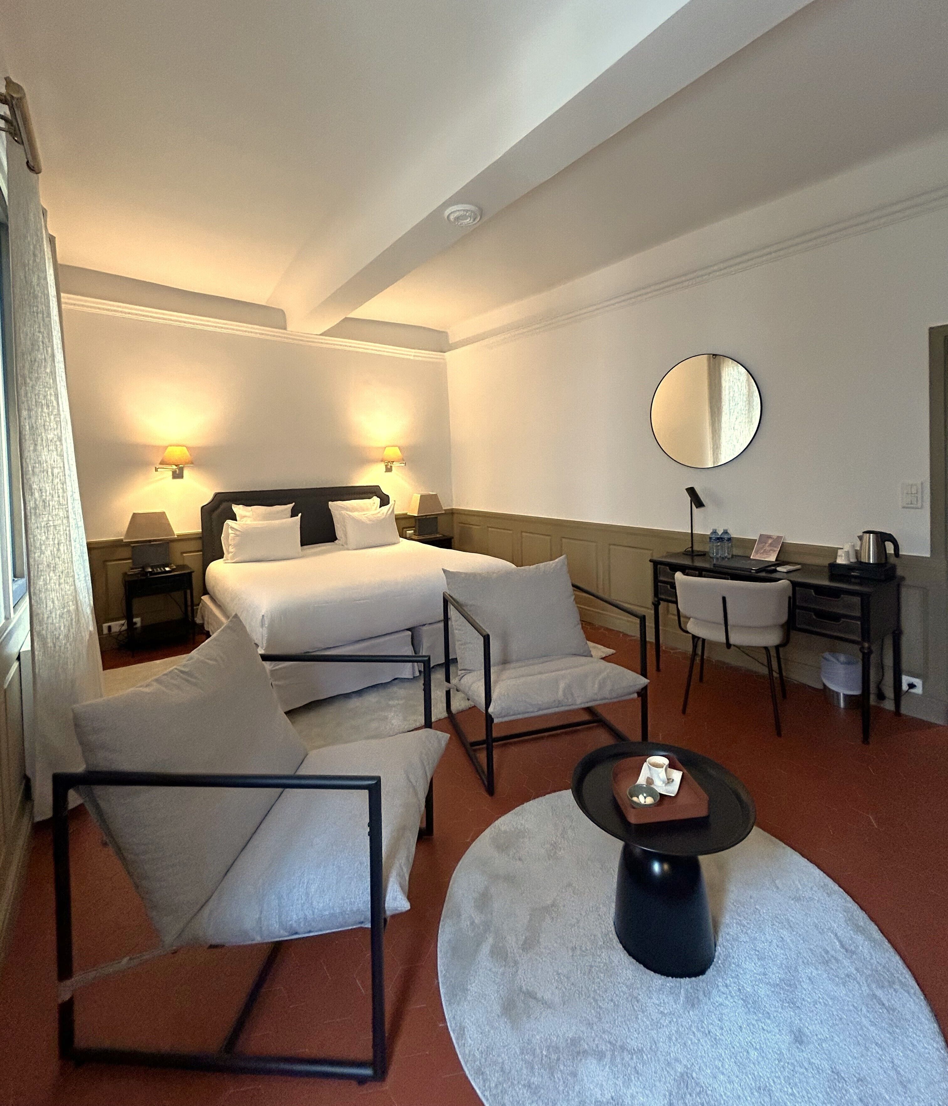 A hotel room with two beds, a desk, a chair, a round coffee table, and a large mirror.