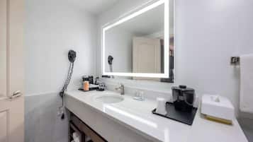 A modern bathroom with a white sink, a large mirror, and a hairdryer on the wall.