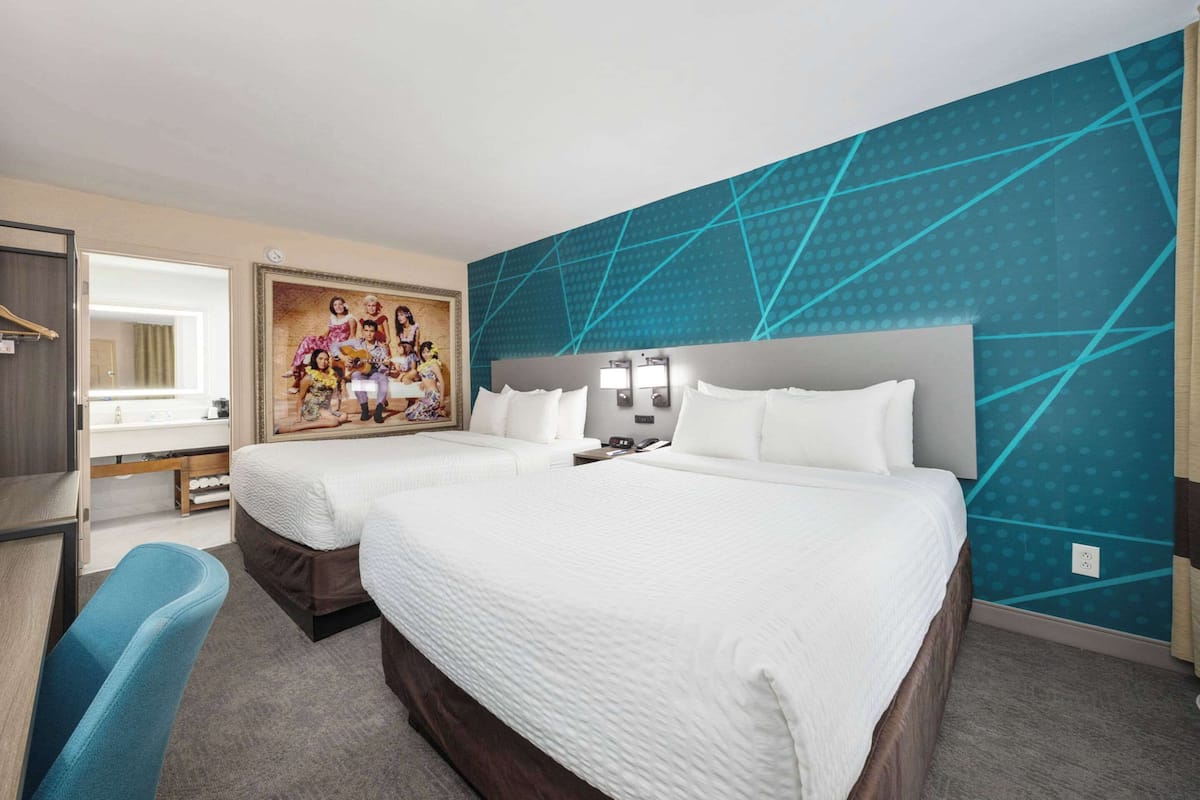 Een hotelkamer met twee bedden, een groot muurschildering, een bureau en een stoel.