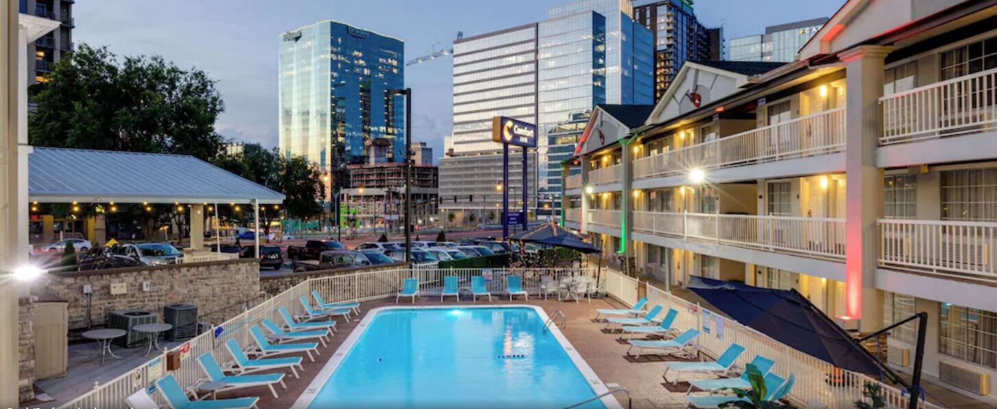 Un hotel con piscina en la azotea rodeada de sillones de descanso, un muro de piedra y vistas a edificios de la ciudad.
