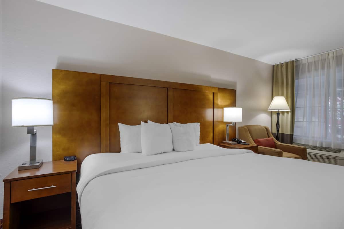 Een hotelkamer met een groot bed, twee nachtkastjes met lampen, een stoel en een raam met gordijnen.