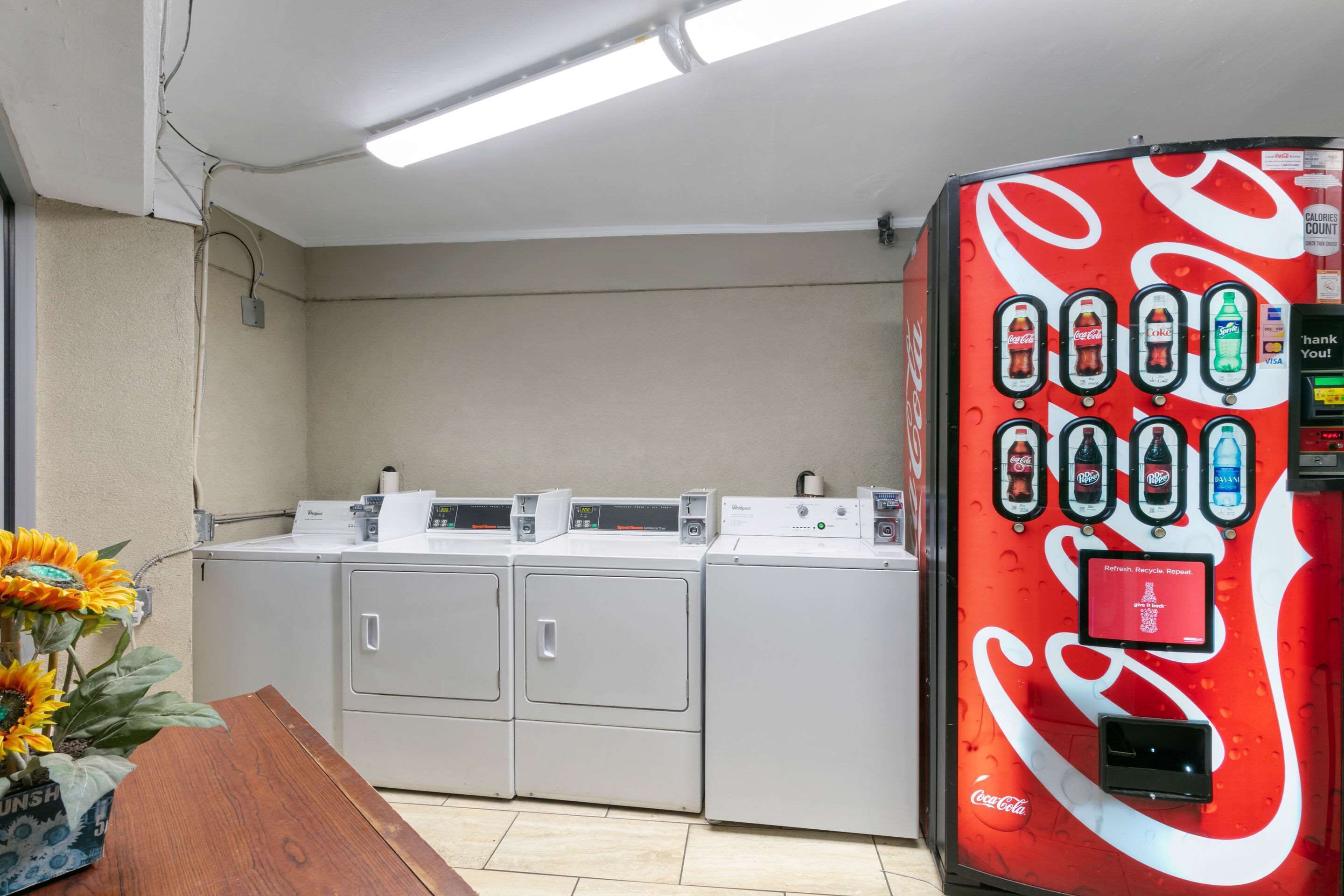A laundry area with four washing machines and a Coca-Cola branded vending machine.