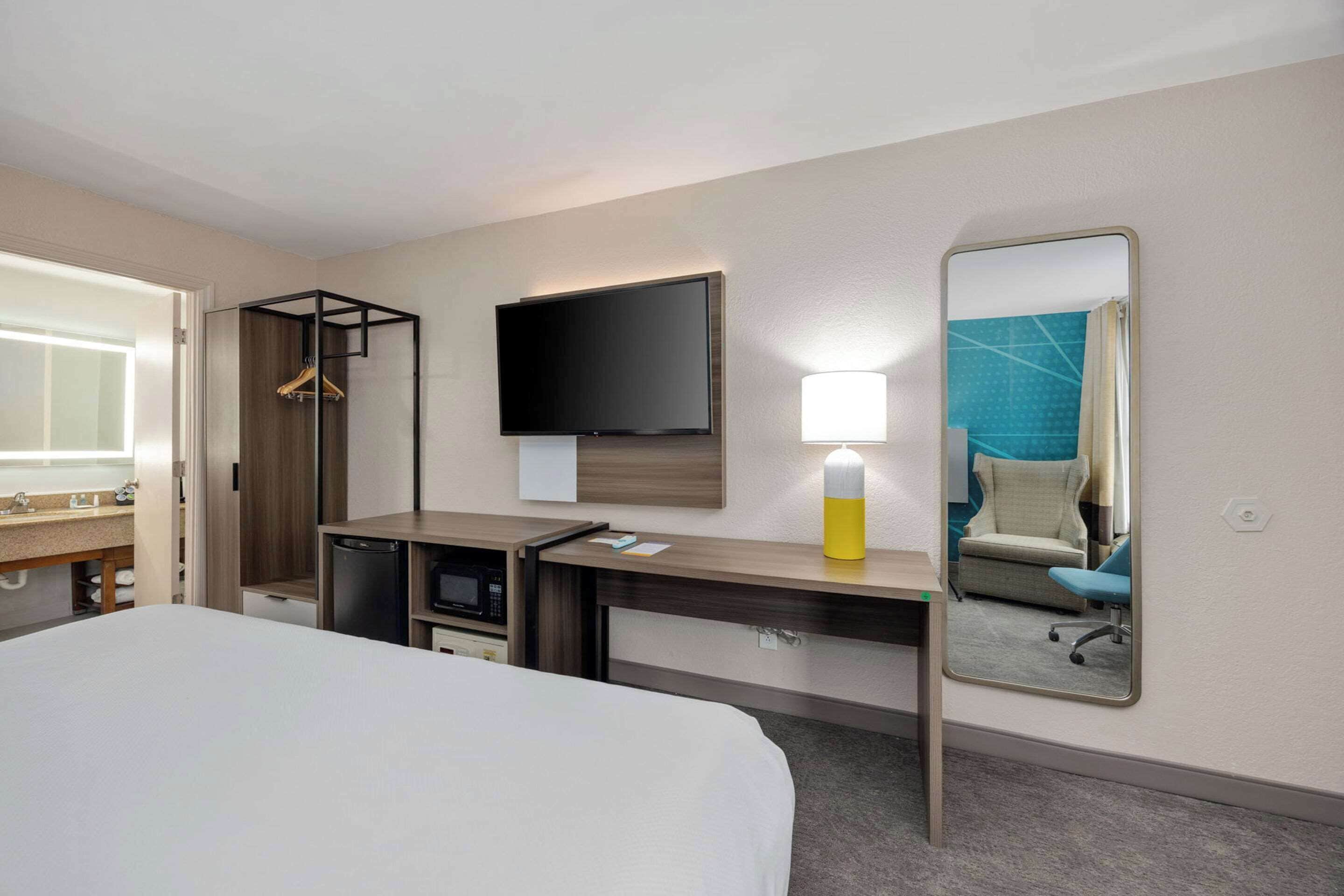 A hotel room with a bed, a desk with a flat-screen TV, a mirror, a lamp, and a microwave.