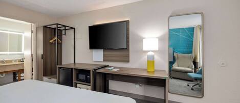 A hotel room with a bed, a desk with a flat-screen TV, a mirror, a lamp, and a microwave.
