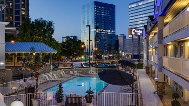 A hotel with a rooftop pool, outdoor seating, and a view of city buildings.
