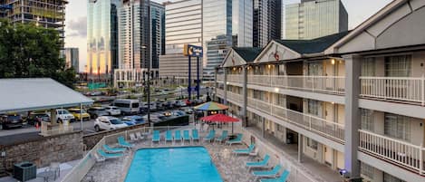 A hotel with a pool, outdoor seating, and a view of the city skyline.