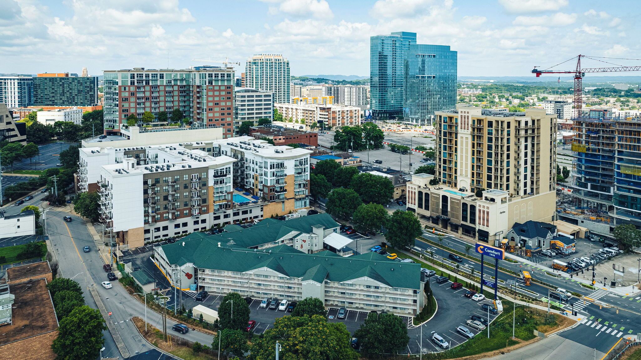 A multi-story hotel with a green roof, located near a busy intersection with visible roadways and construction cranes.