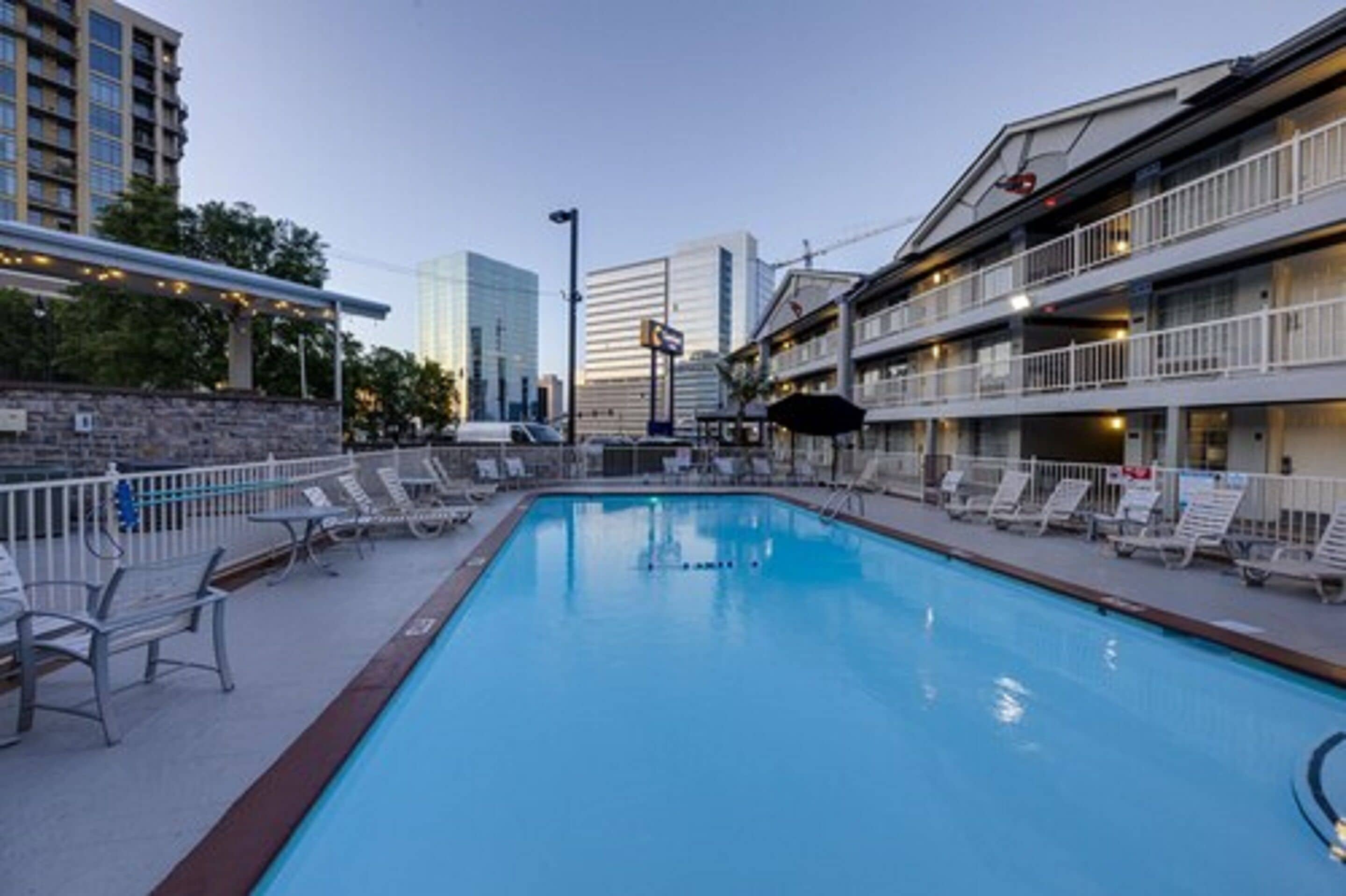 Une piscine avec des chaises longues, un mur en pierre et un bâtiment doté de balcons en arrière-plan.