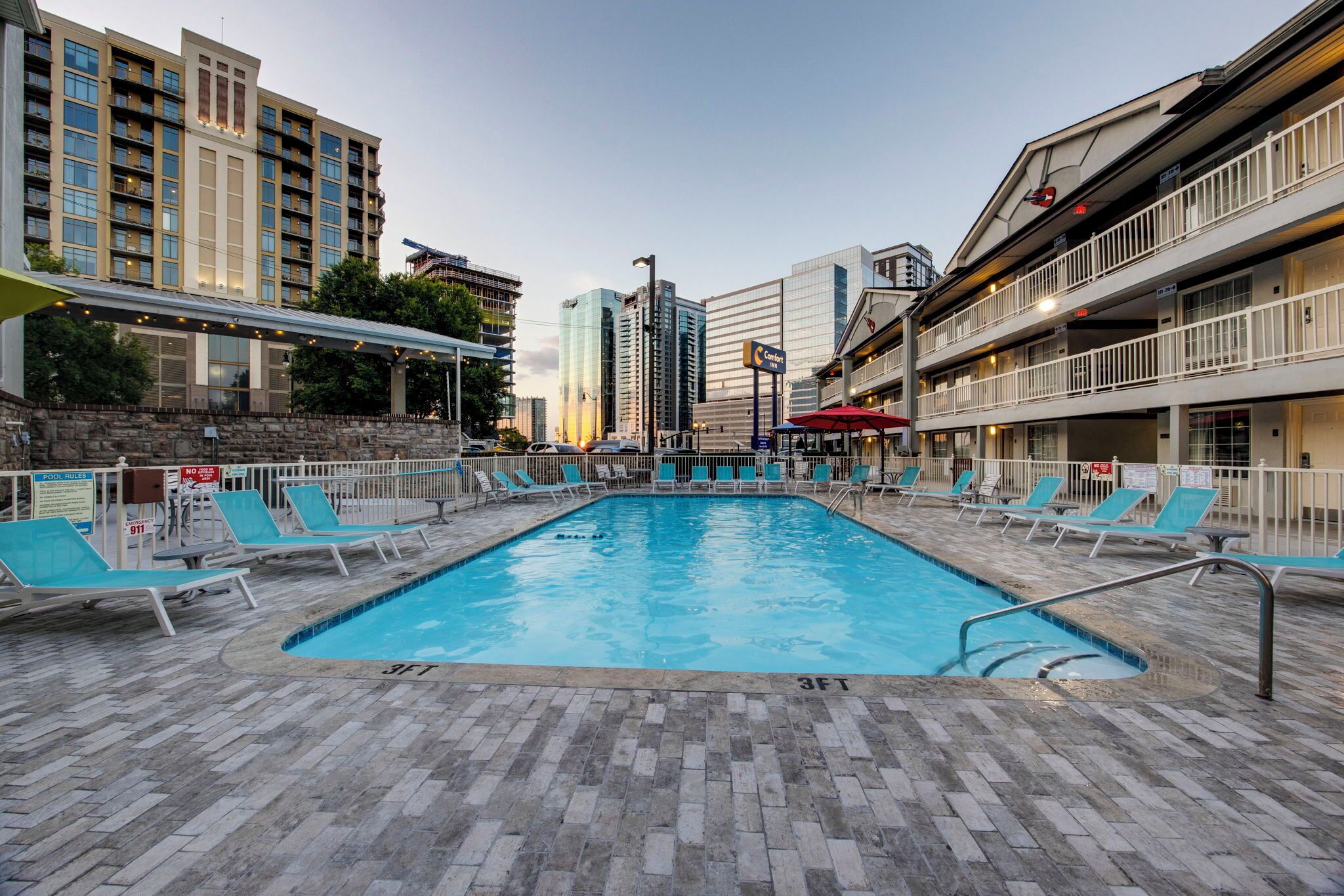 A swimming pool with lounge chairs, surrounded by buildings and a covered area.