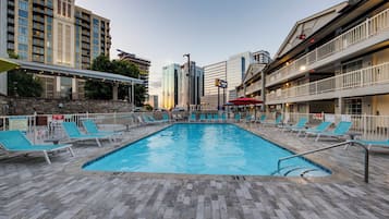 Una piscina con sillas de descanso, rodeada de edificios y una zona cubierta.