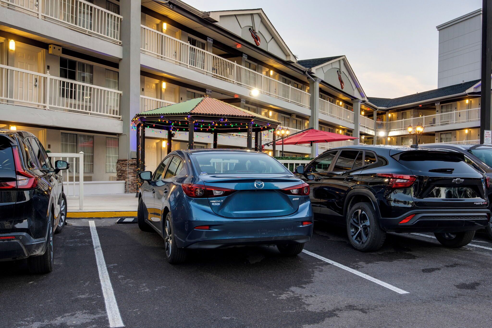 A parking lot with several cars, a building with multiple balconies, and a gazebo with colorful lights.
