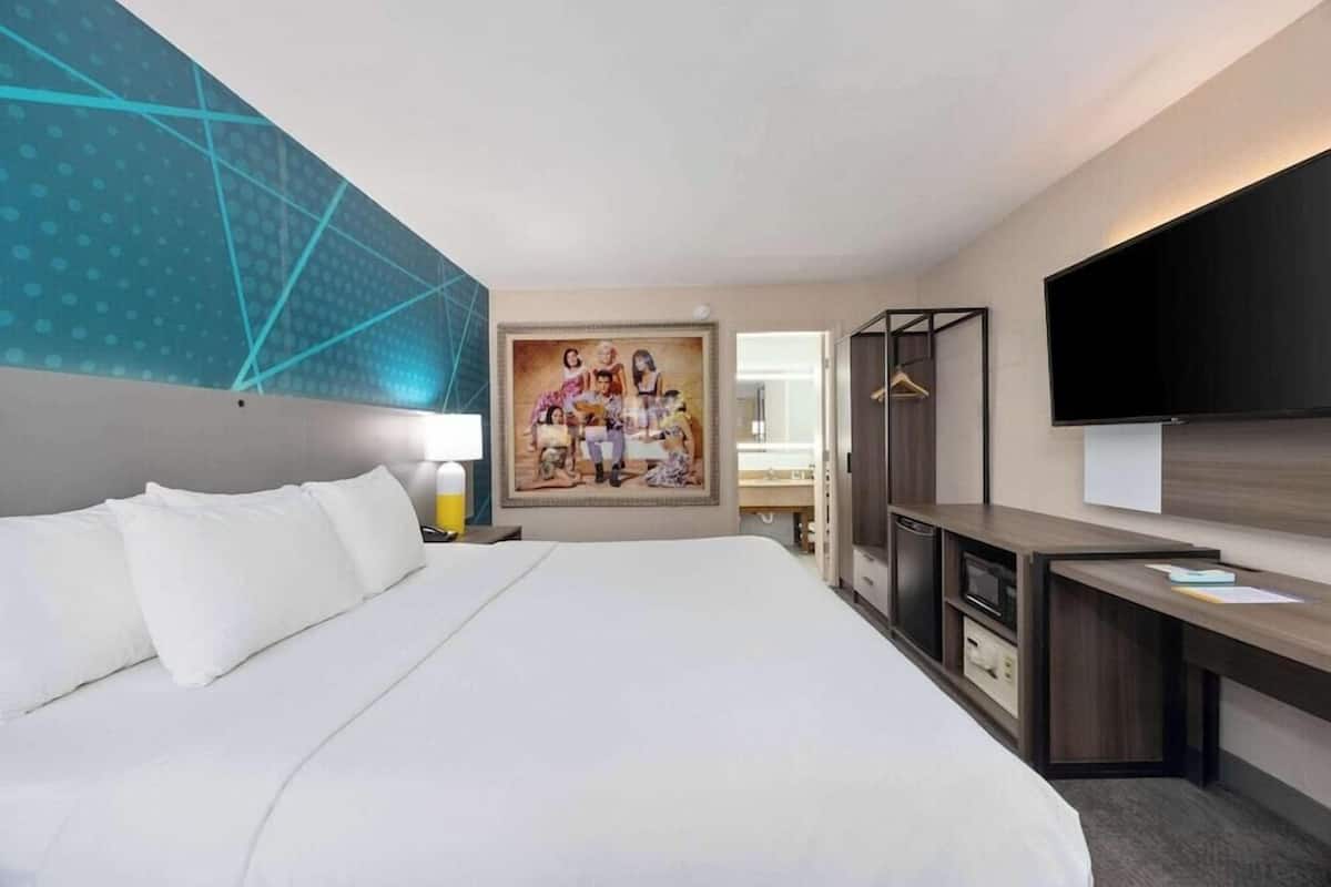 Een hotelkamer met een bed, een bureau, een televisie, een schilderij en een kledingkast.