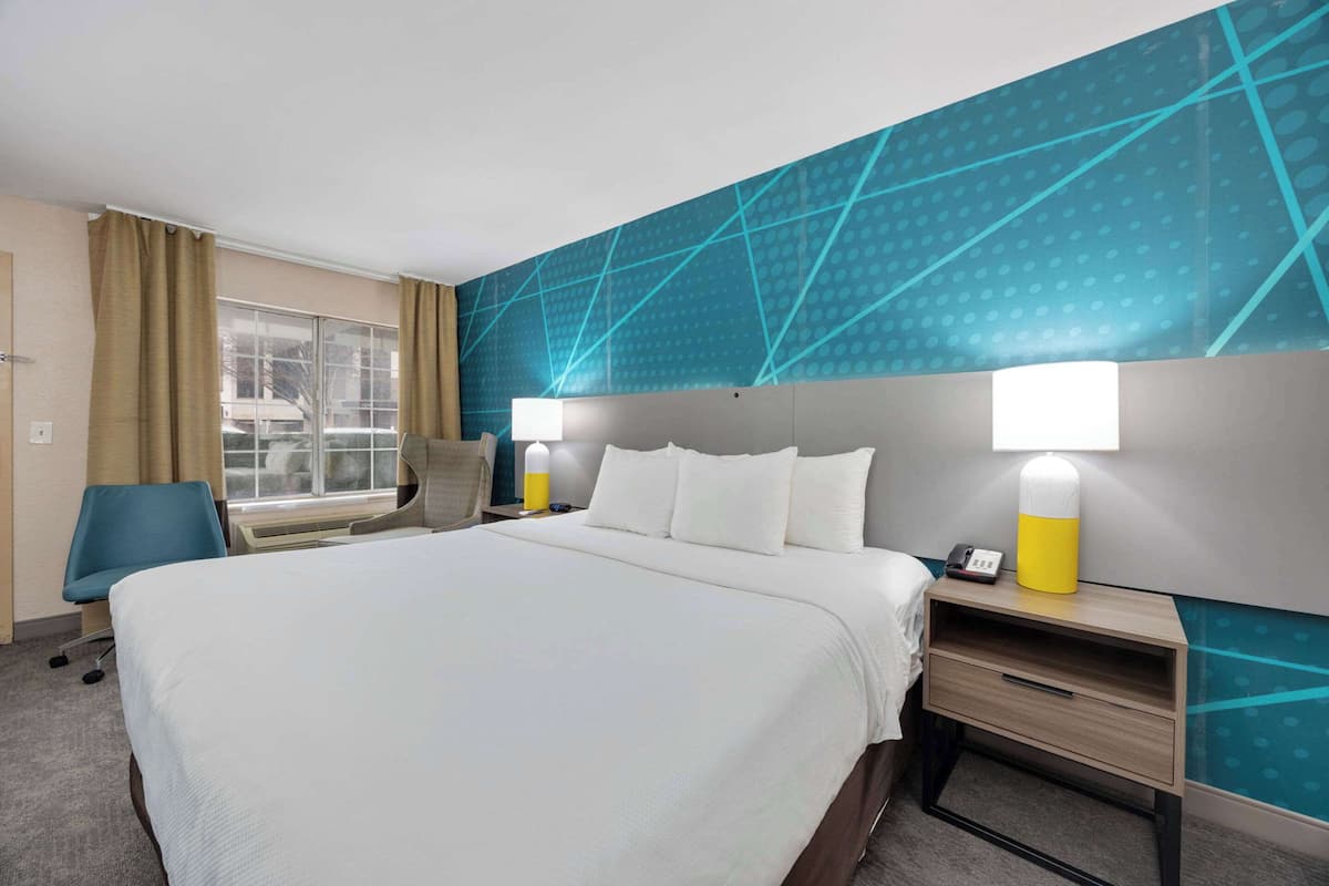 Een hotelkamer met een groot bed, twee nachtkastjes met lampen, een stoel en een raam met gordijnen.