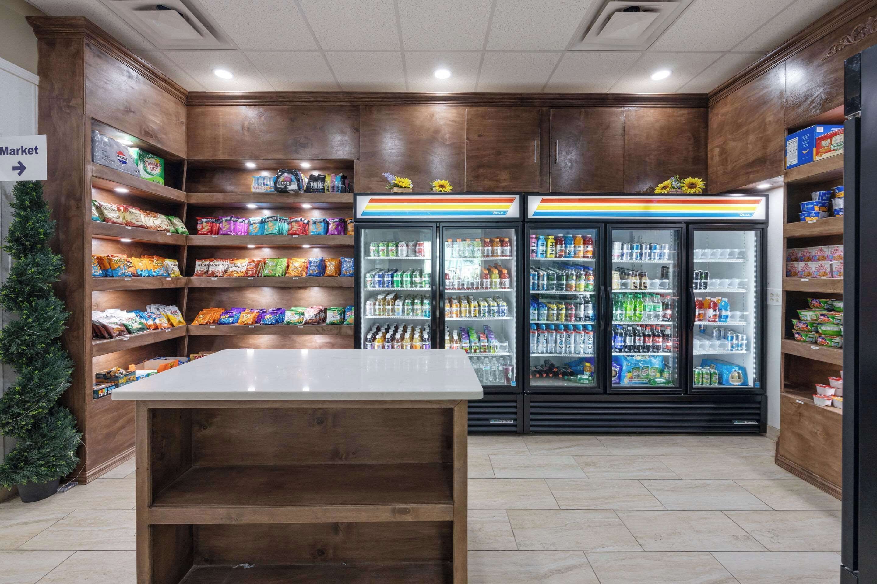 A grocery store interior with wooden shelving, a central white table, and refrigerated beverage cases.