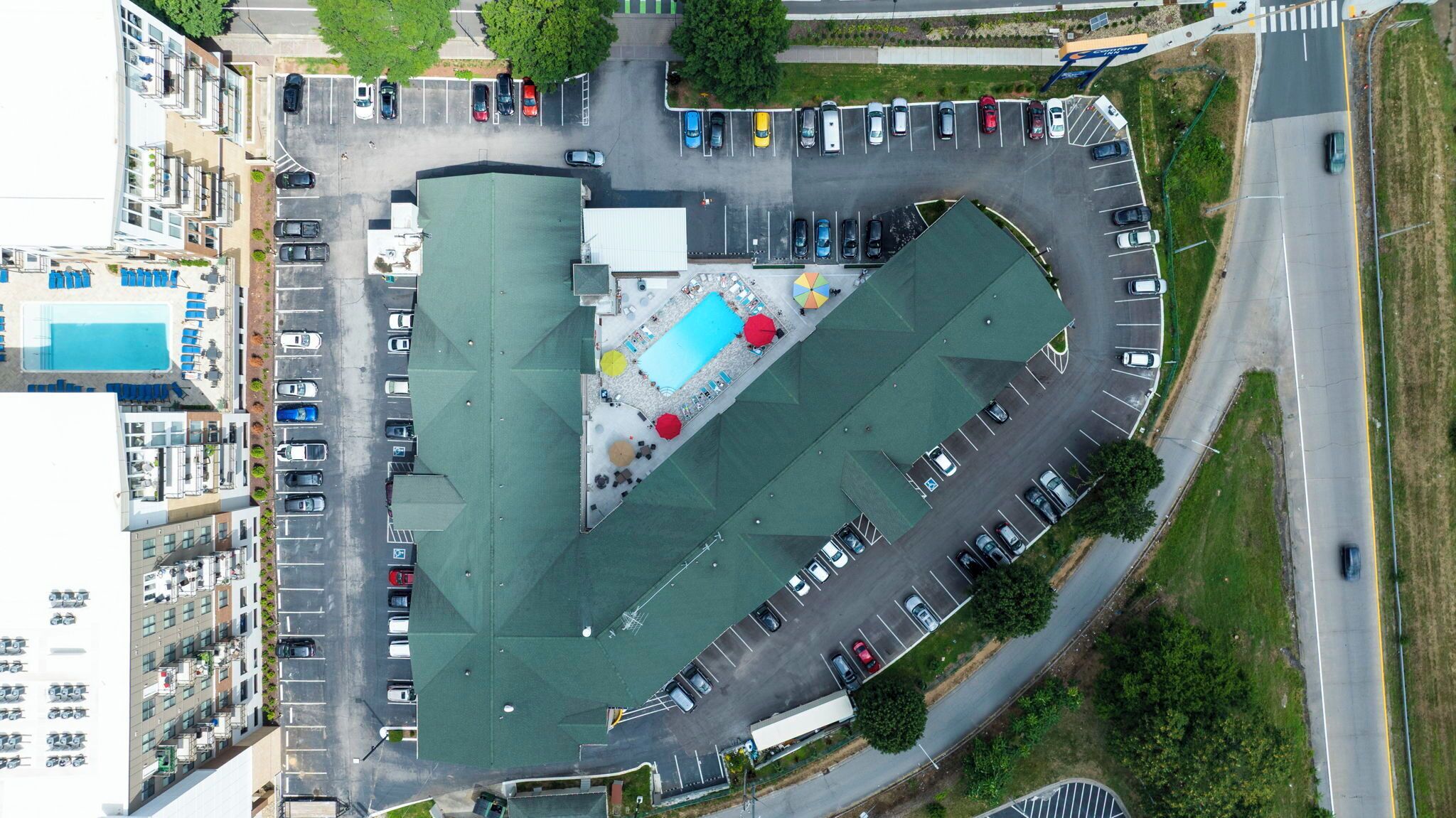 Vista aérea de un estacionamiento con múltiples filas de coches, una piscina y un edificio con techo verde.