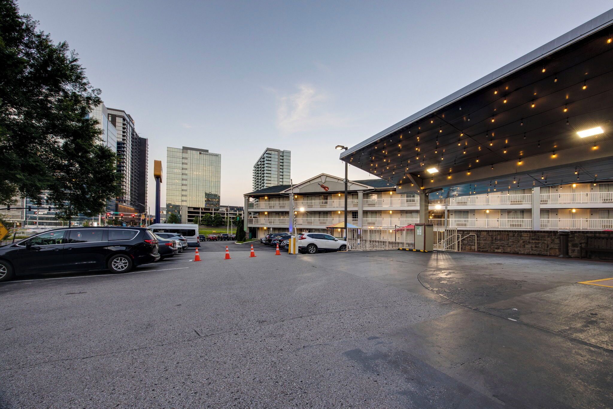 A hotel with a covered outdoor area, multiple floors, and a parking lot with cars and traffic cones.