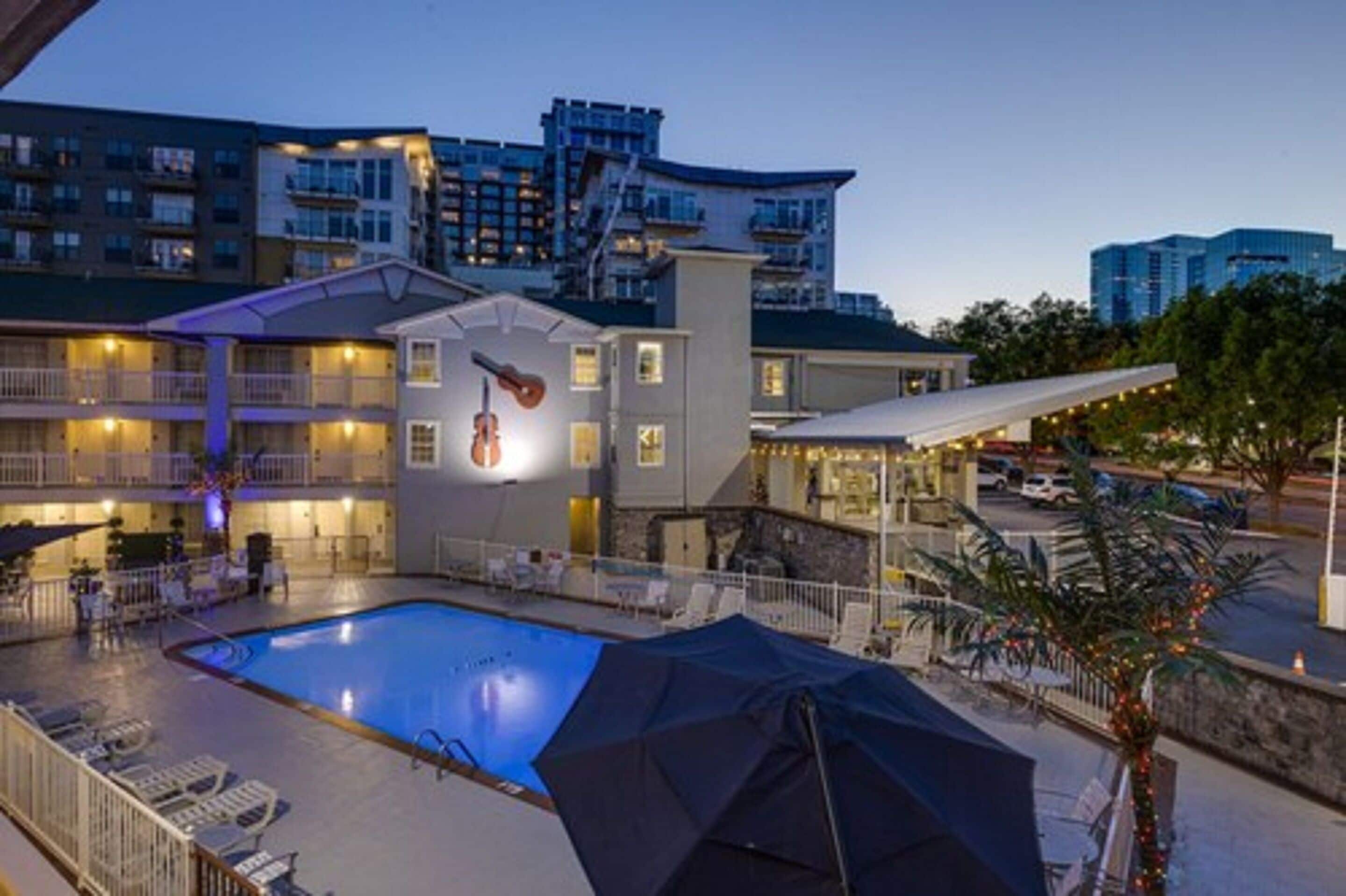 A hotel with a swimming pool, outdoor seating, and a covered area with string lights.