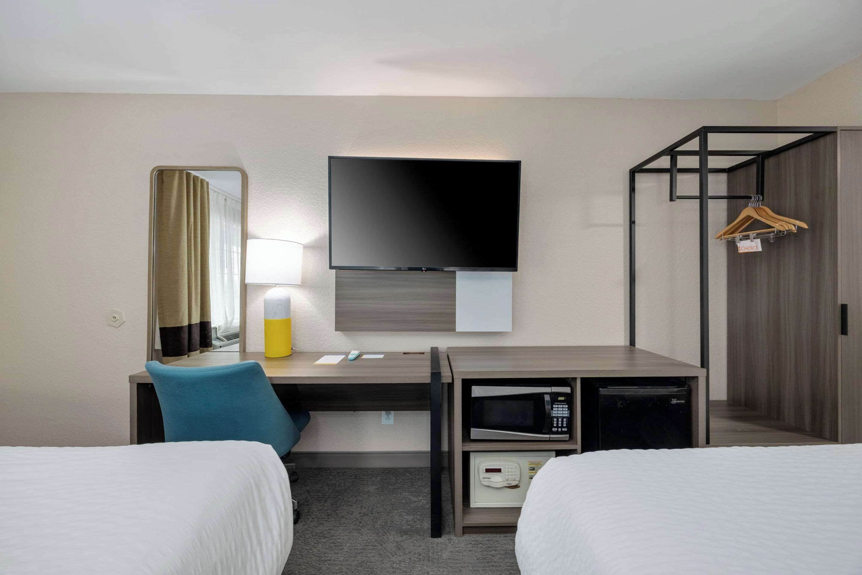 Une chambre d’hôtel comprenant un lit, un bureau avec une chaise, un téléviseur à écran plat, un four à micro-ondes et une armoire.