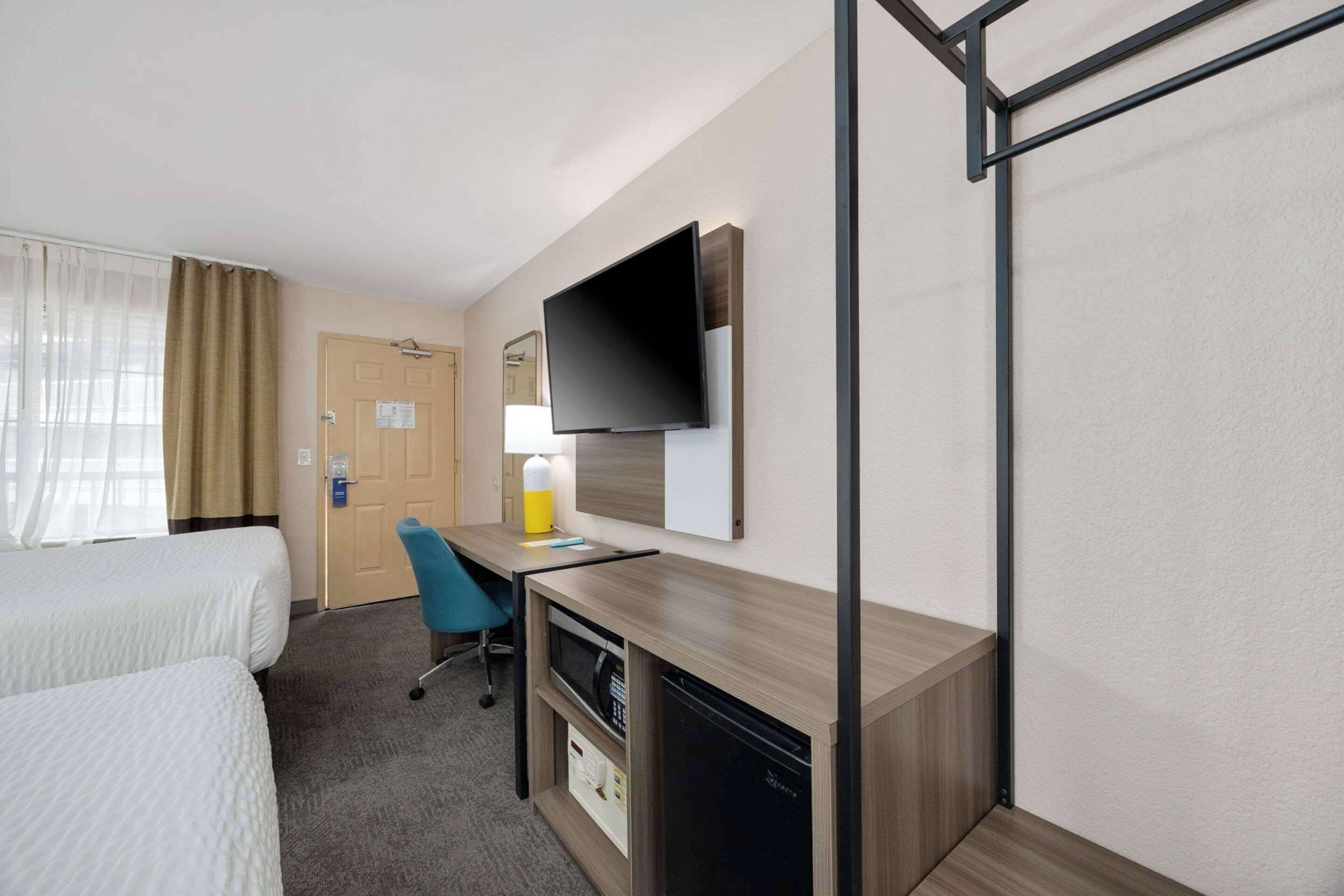 Ein Hotelzimmer mit zwei Betten, einem Schreibtisch mit Lampe, einem Fernseher und einer Mikrowelle.