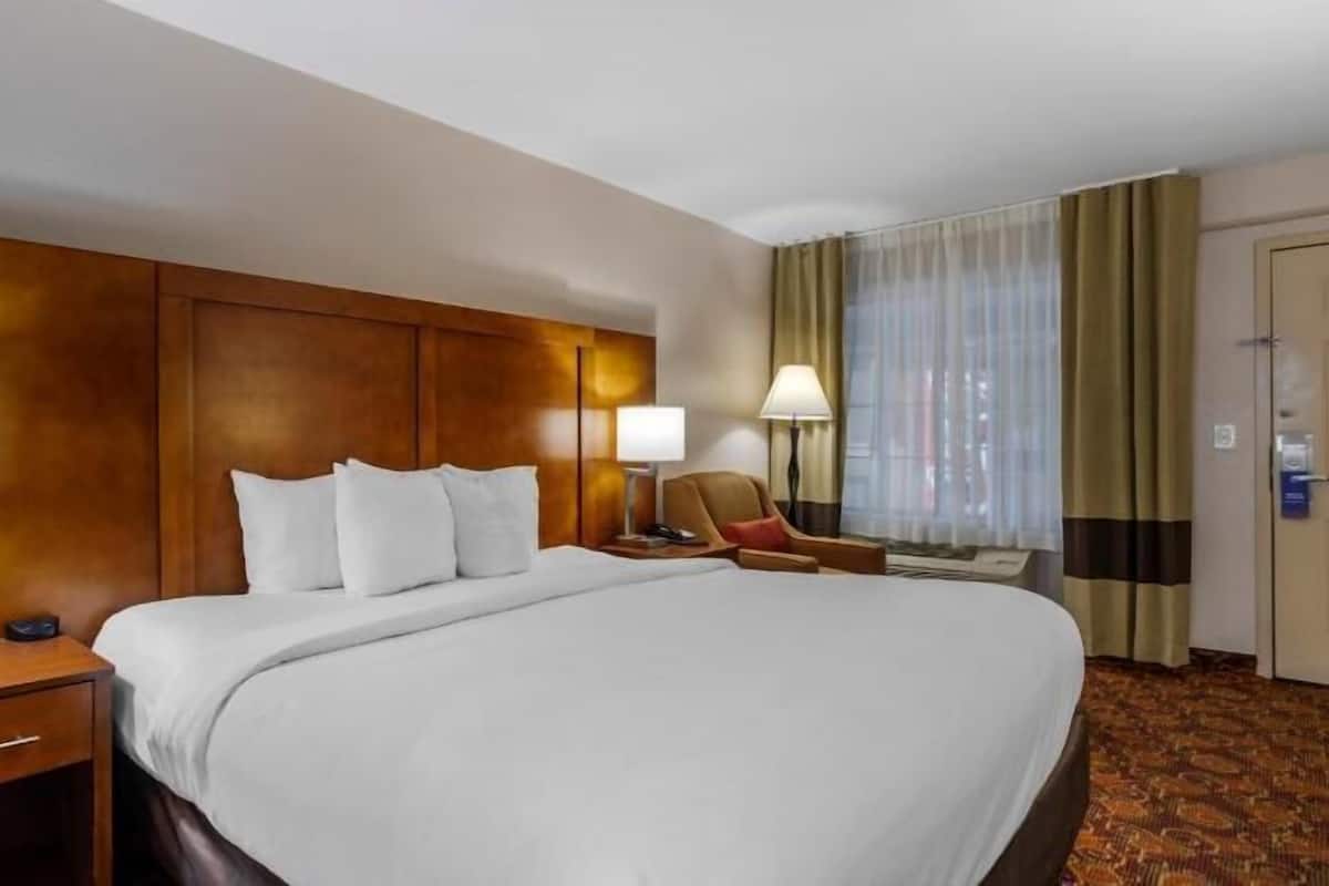 Een hotelkamer met een groot bed, twee nachtkastjes met lampen, een stoel en een deur.