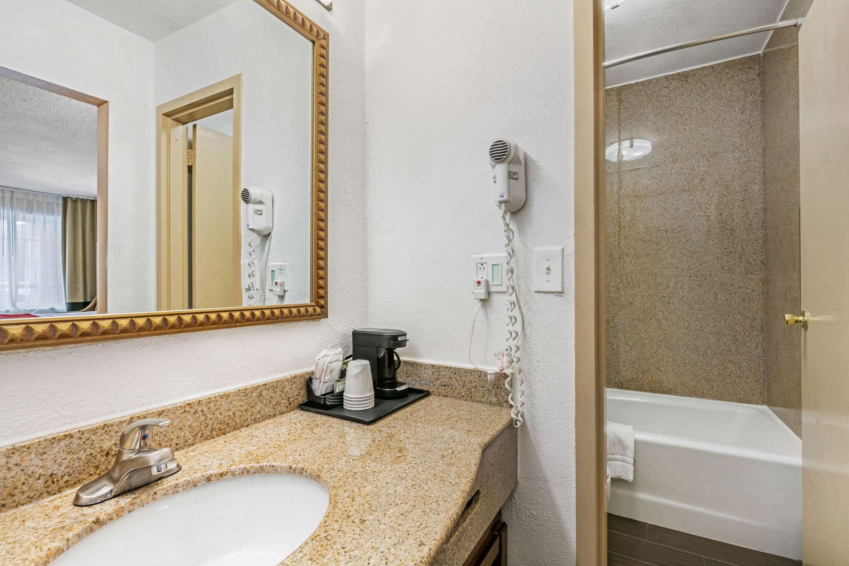 Une salle de bain d’hôtel équipée d’un lavabo, d’un miroir, d’un sèche-cheveux et d’une baignoire.