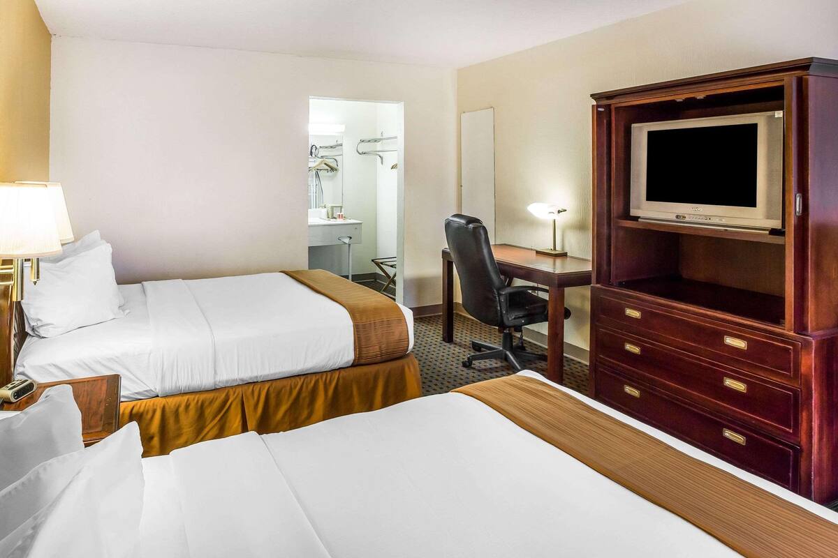 A hotel room with two beds, a desk, a chair, a television, and a mirror.