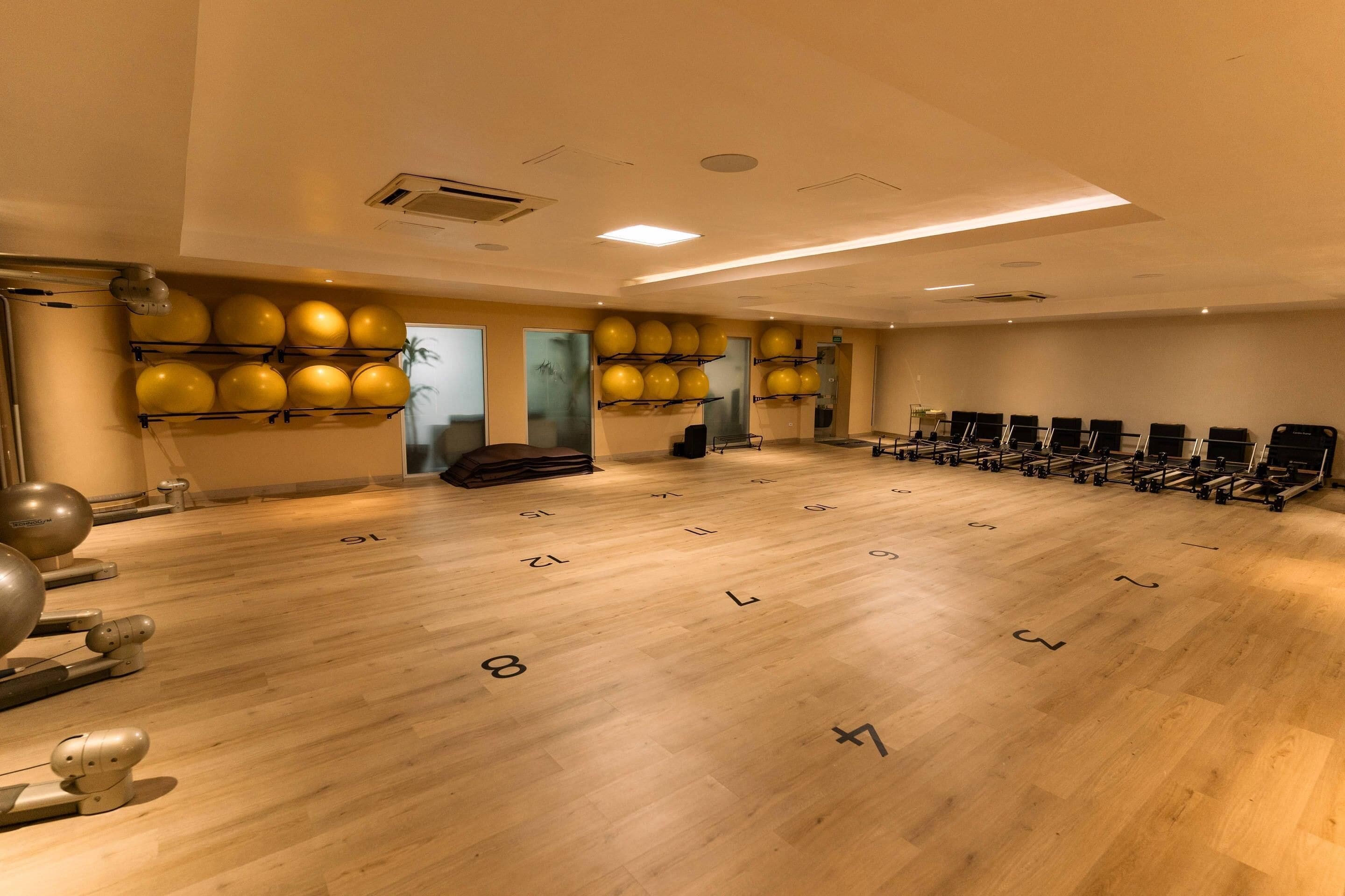 Uma academia com equipamentos de exercício, colchonetes numerados e bolas de ginástica amarelas.
