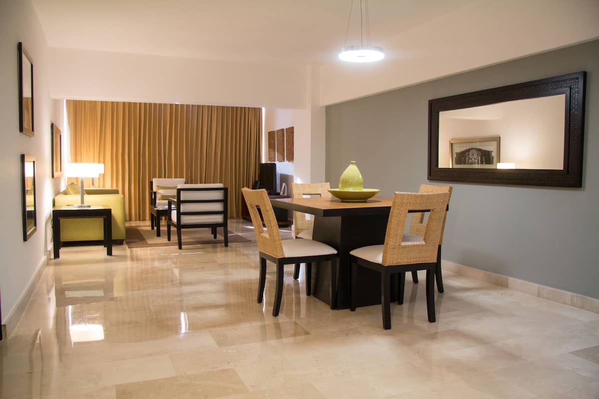 A hotel dining area with a table and chairs, a lamp, and a large mirror on the wall.