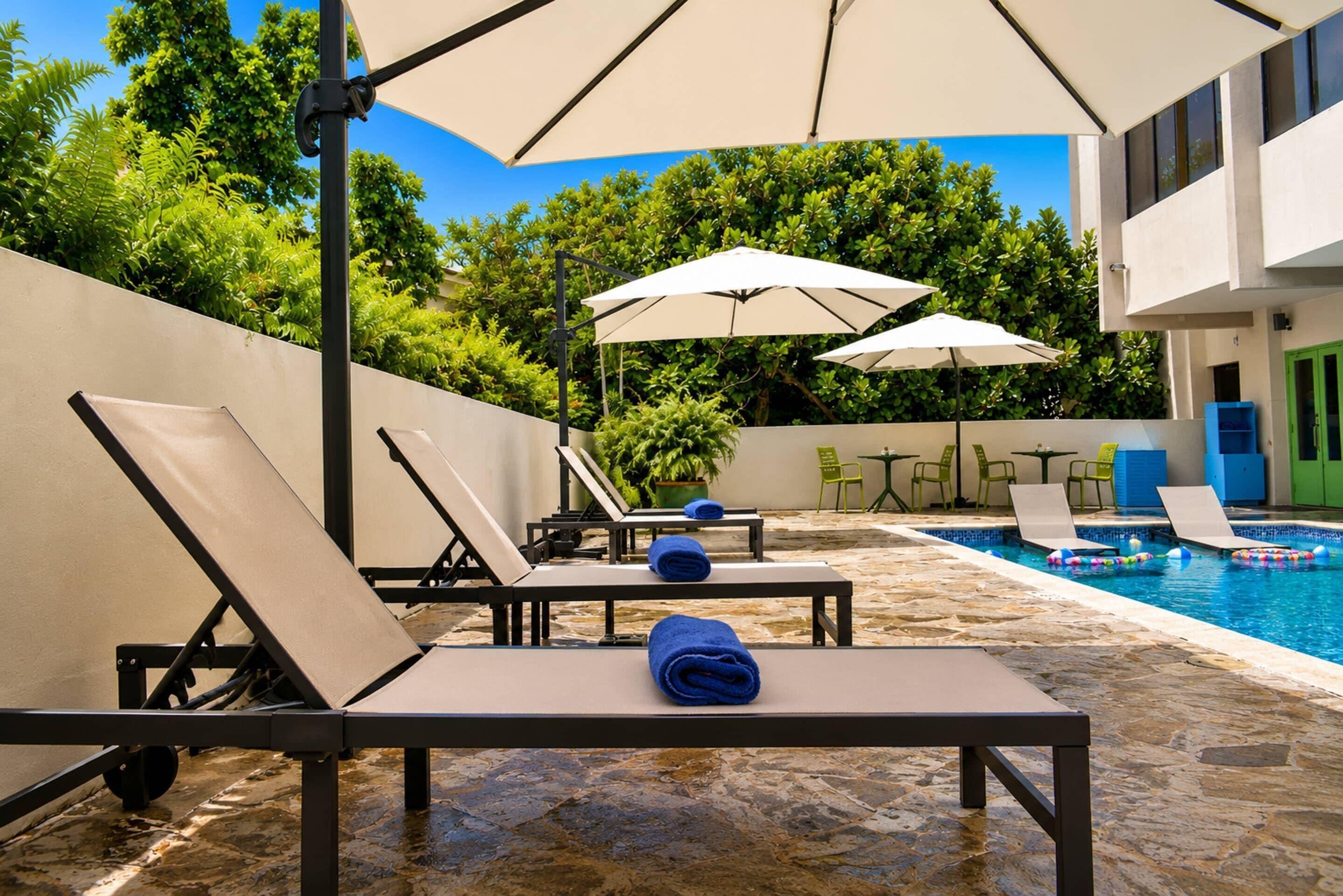 A poolside area with lounge chairs and umbrellas, a pool, and a stone-tiled deck.
