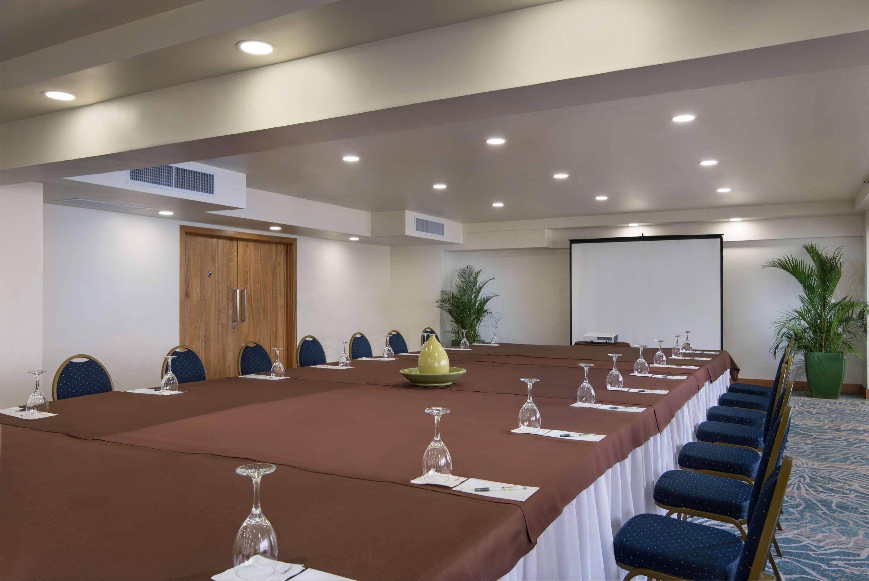 A conference room with a long table, chairs, a projector screen, and a door.