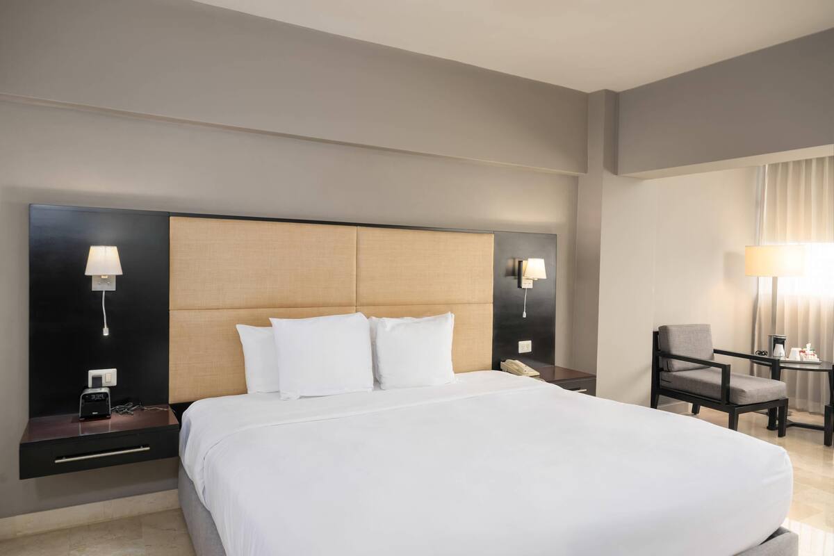 A hotel room with a large bed, bedside tables, a chair, and a desk with a lamp.