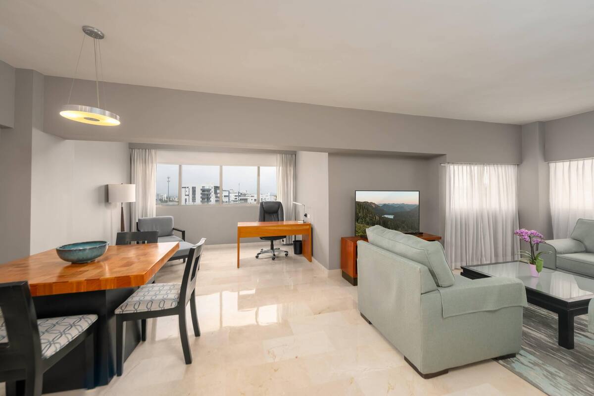 A modern living room with a dining area, a sofa, a TV, and a city view.