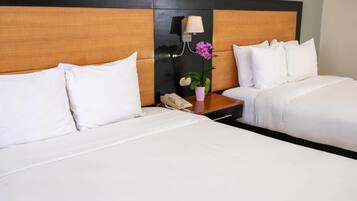 Habitación de hotel con dos camas, una mesita de noche, una lámpara, un teléfono y una orquídea en maceta.