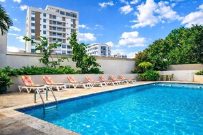 A swimming pool with lounge chairs, surrounded by greenery and modern buildings. - Radisson Hotel Santo Domingo (Santo Domingo)