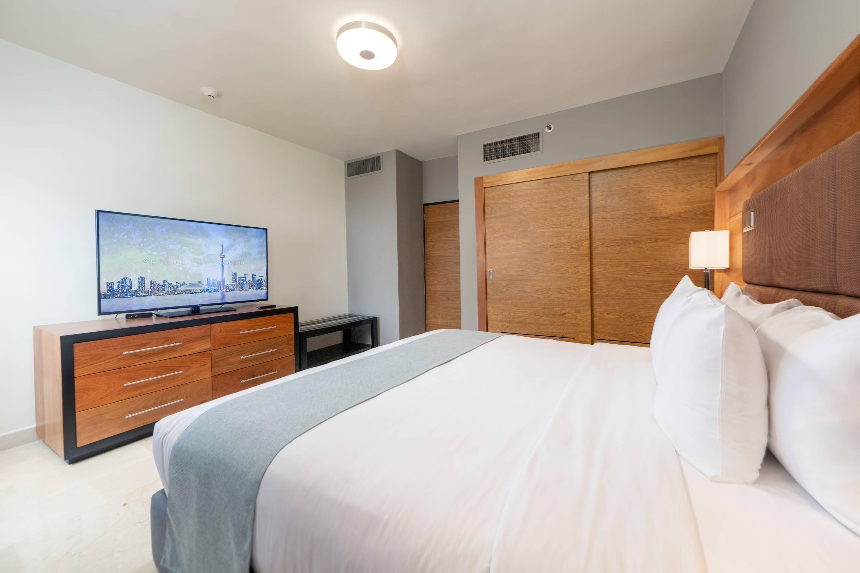 Et hotelværelse med en seng, et fjernsyn på en trækommode, et garderobeskab og en lampe.