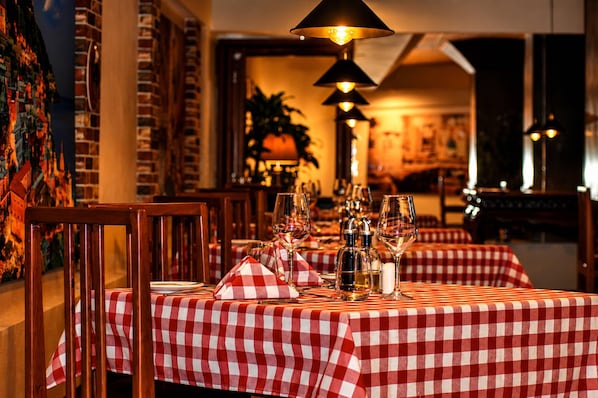 A restaurant interior with checkered tablecloths, wine glasses, and bottles, and a warm ambient lighting.