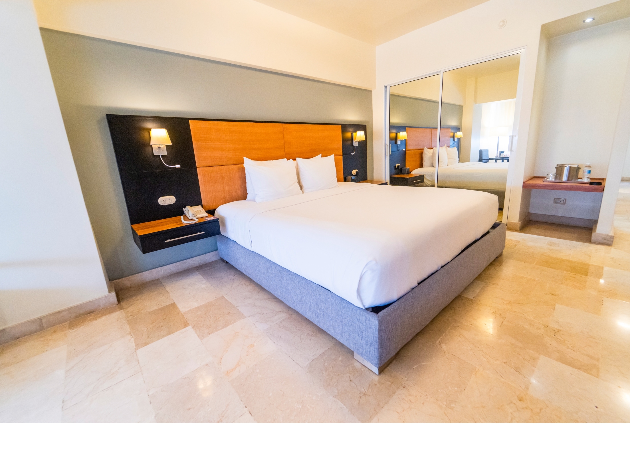 Una habitación de hotel moderna con una cama grande, una mesita de noche, un espejo y una pequeña mesa.