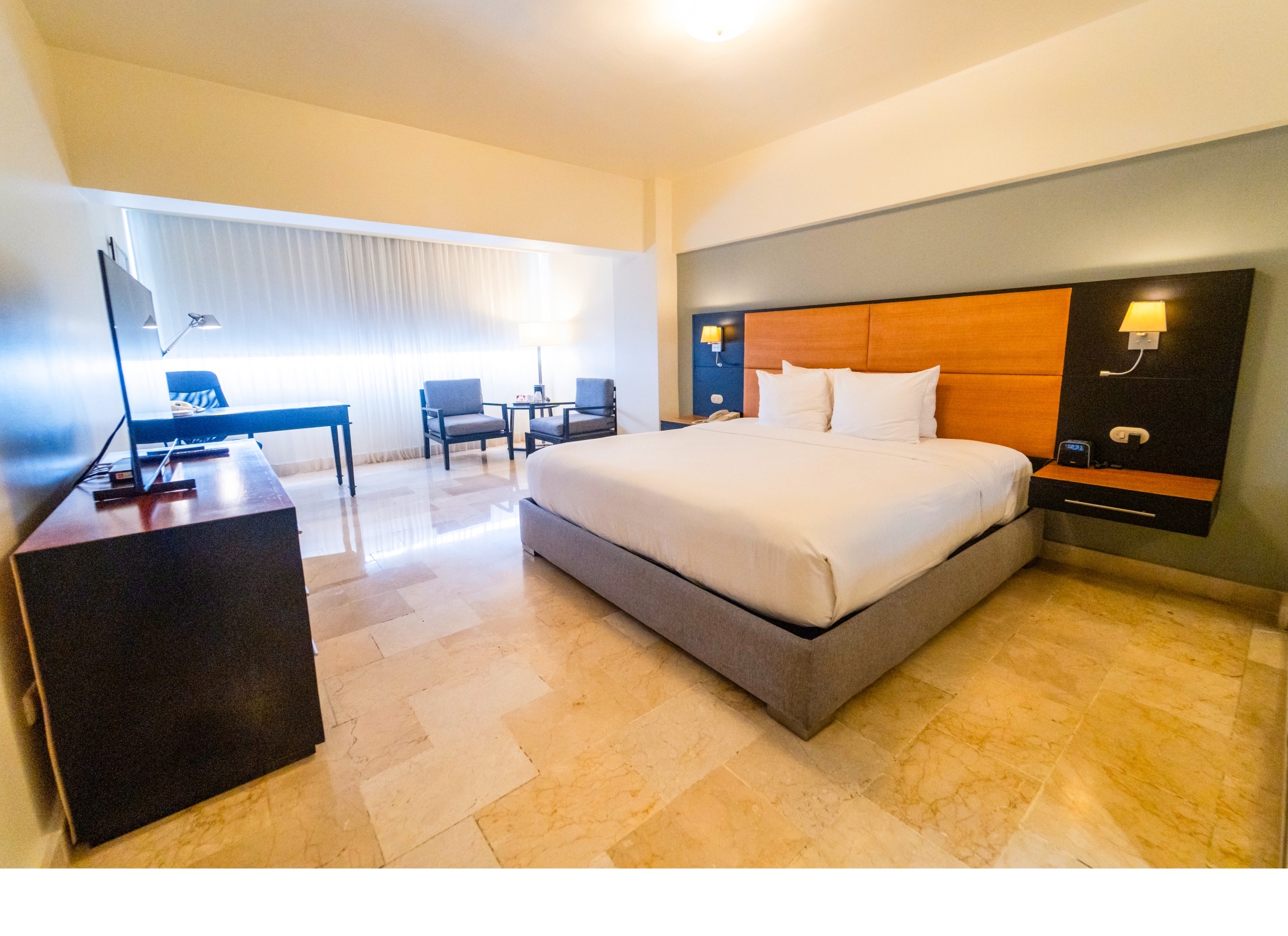 A modern hotel room with a large bed, a desk, and a chair.