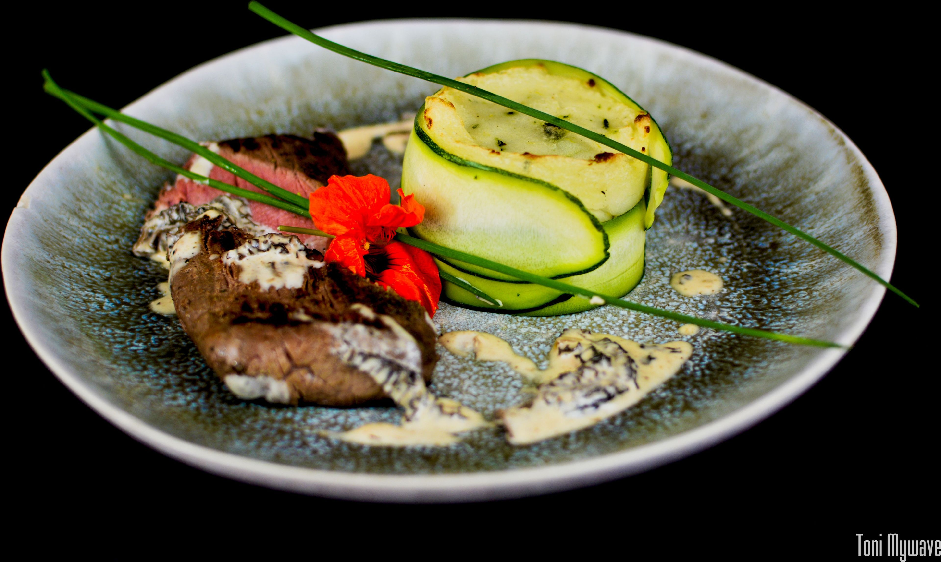 A plate with grilled meat, zucchini slices, and a red flower garnish.