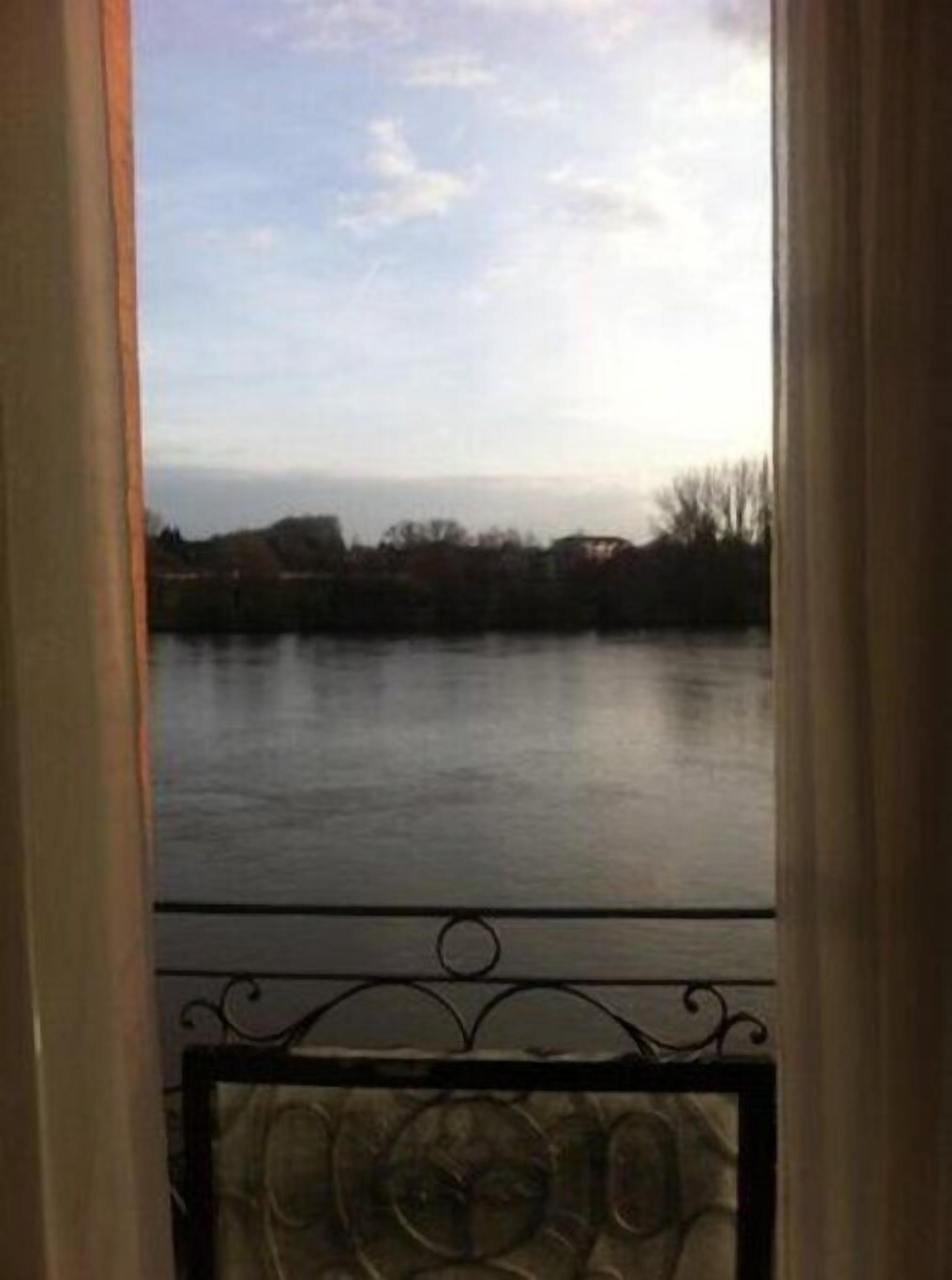 A view from a balcony with a metal railing overlooking a calm body of water and distant buildings.