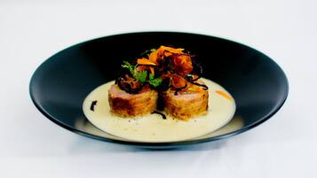 A black plate with a white sauce and two pieces of food topped with vegetables and herbs.