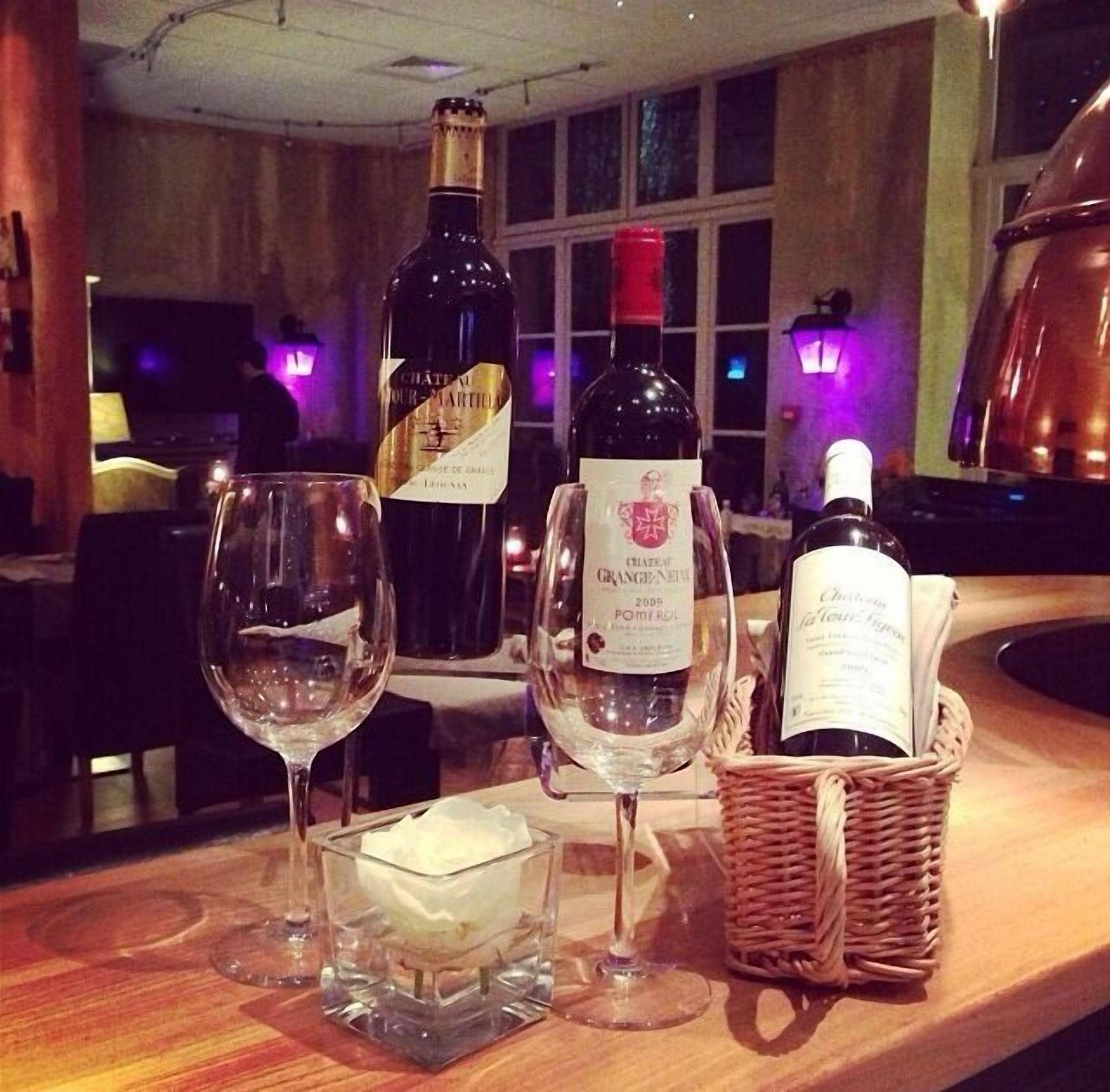 Une table avec trois bouteilles de vin, deux verres et une bougie.