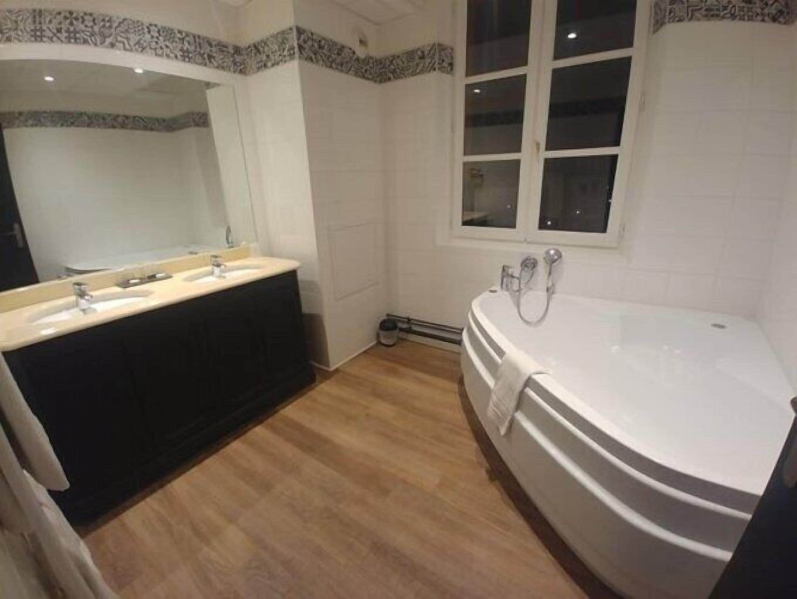 A bathroom with a double sink vanity, a large freestanding bathtub, and a window above the bathtub.