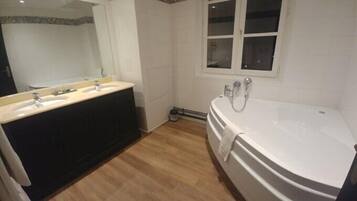 A bathroom with a double sink vanity, a large freestanding bathtub, and a window above the bathtub.