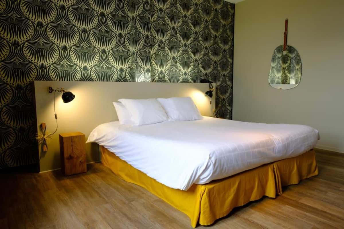 Cama bem arrumada com roupa de cama branca, mesa de cabeceira de madeira e espelho fixado na parede.