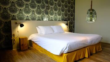 A neatly made bed with a yellow skirt, a wooden nightstand, and a wall-mounted lamp.