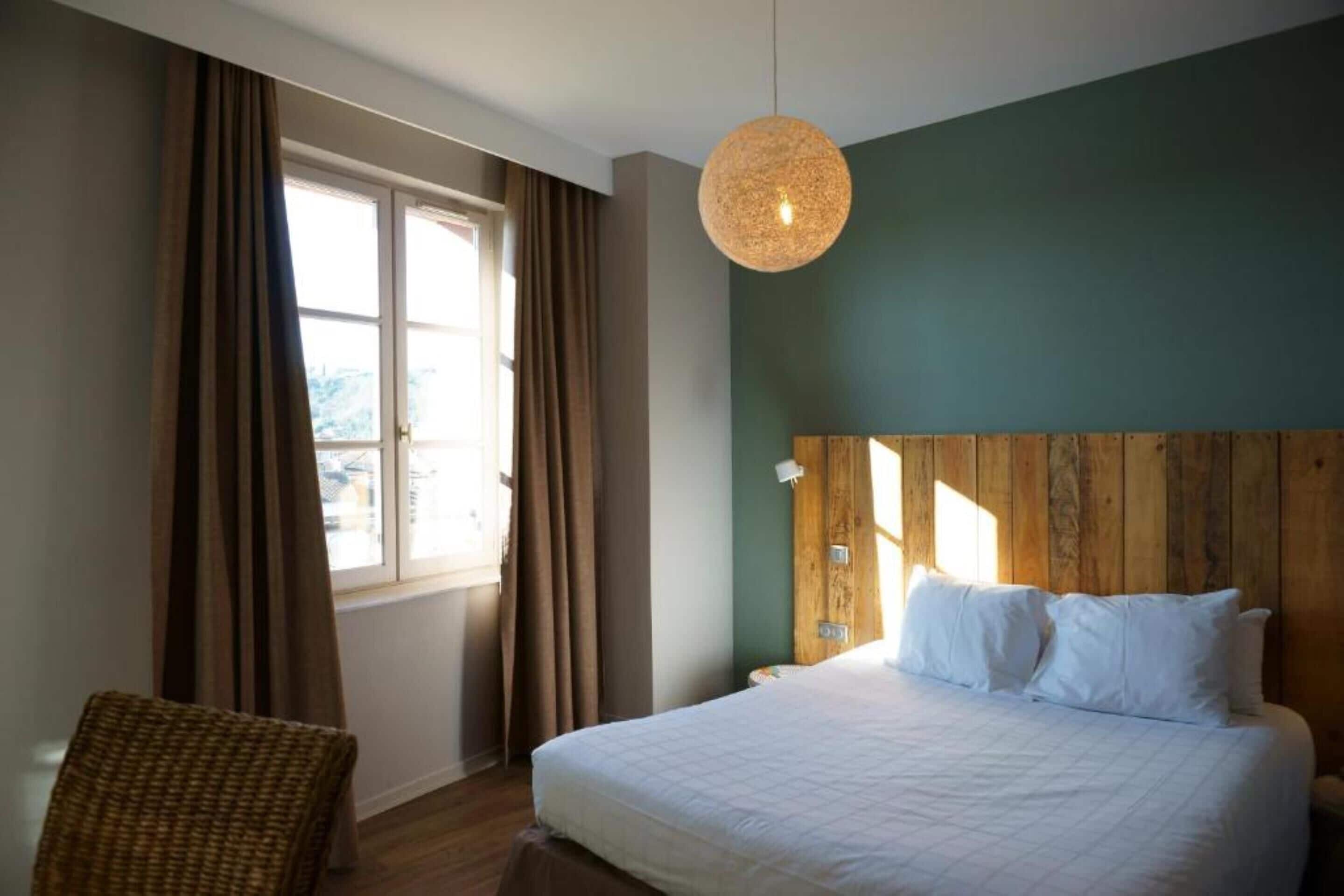 A bedroom with a large bed, a wooden headboard, a hanging light fixture, and a window with curtains.