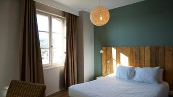 A bedroom with a large bed, a wooden headboard, a hanging light fixture, and a window with curtains.